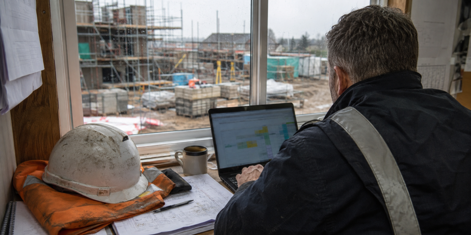 Construction site manager reviewing workforce training requirements on a laptop and tablet.